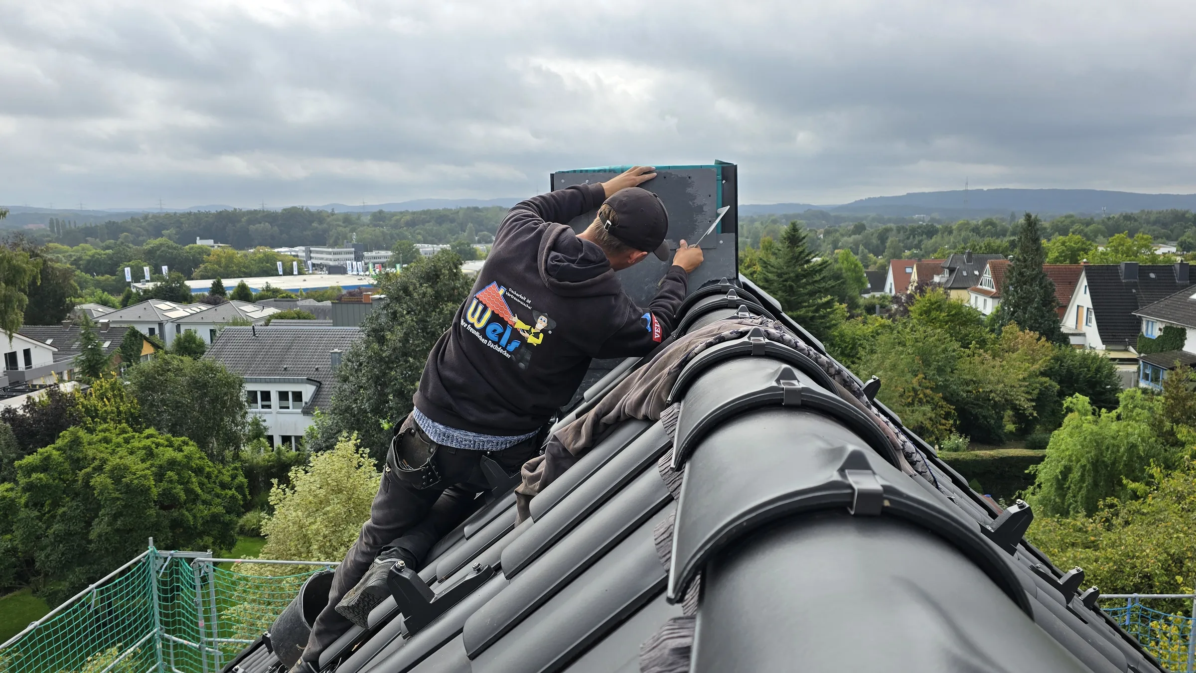 Dachdecker von Wels Bedachungen arbeitet auf dem First, im Hintergrund Osnabrücker Wohngebiet